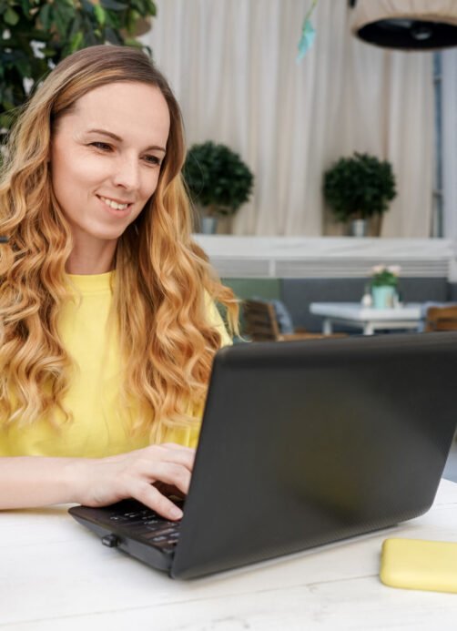 Smiling young female caucasian freelancer is sitting in a street cafe with her netbook.